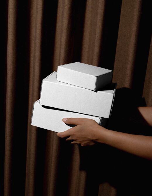 Three blank white boxes stacked in hands with brown curtain backdrop