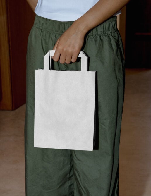 Person holding blank white paper shopping bag with handles against green pants