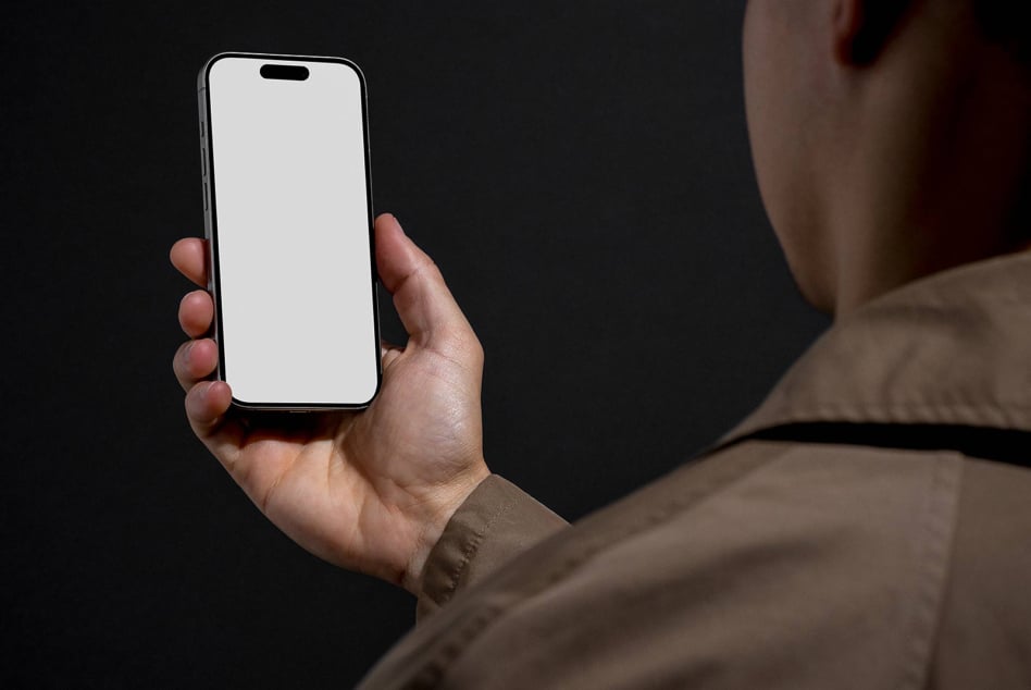 Person in brown jacket holding iPhone with blank white screen on dark background