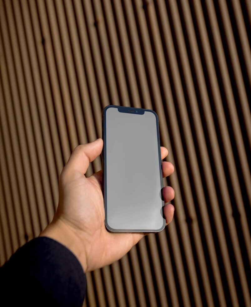 Hand holding blue phone with blank gray screen against wood slat background