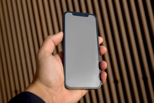 Hand holding dark blue phone with empty gray screen on wood backdrop