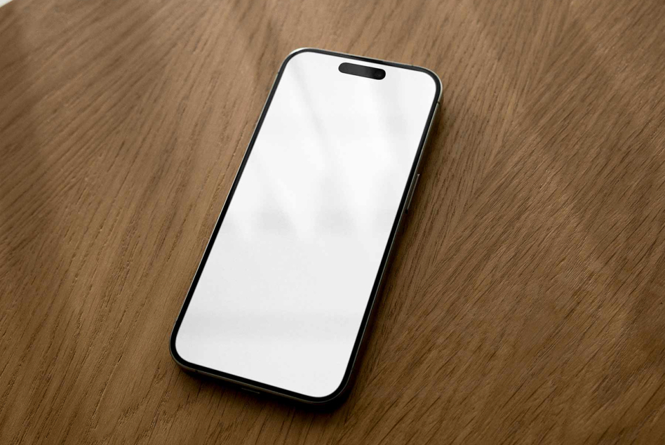 Black iPhone on natural wood table with blank white screen ready for design mockup
