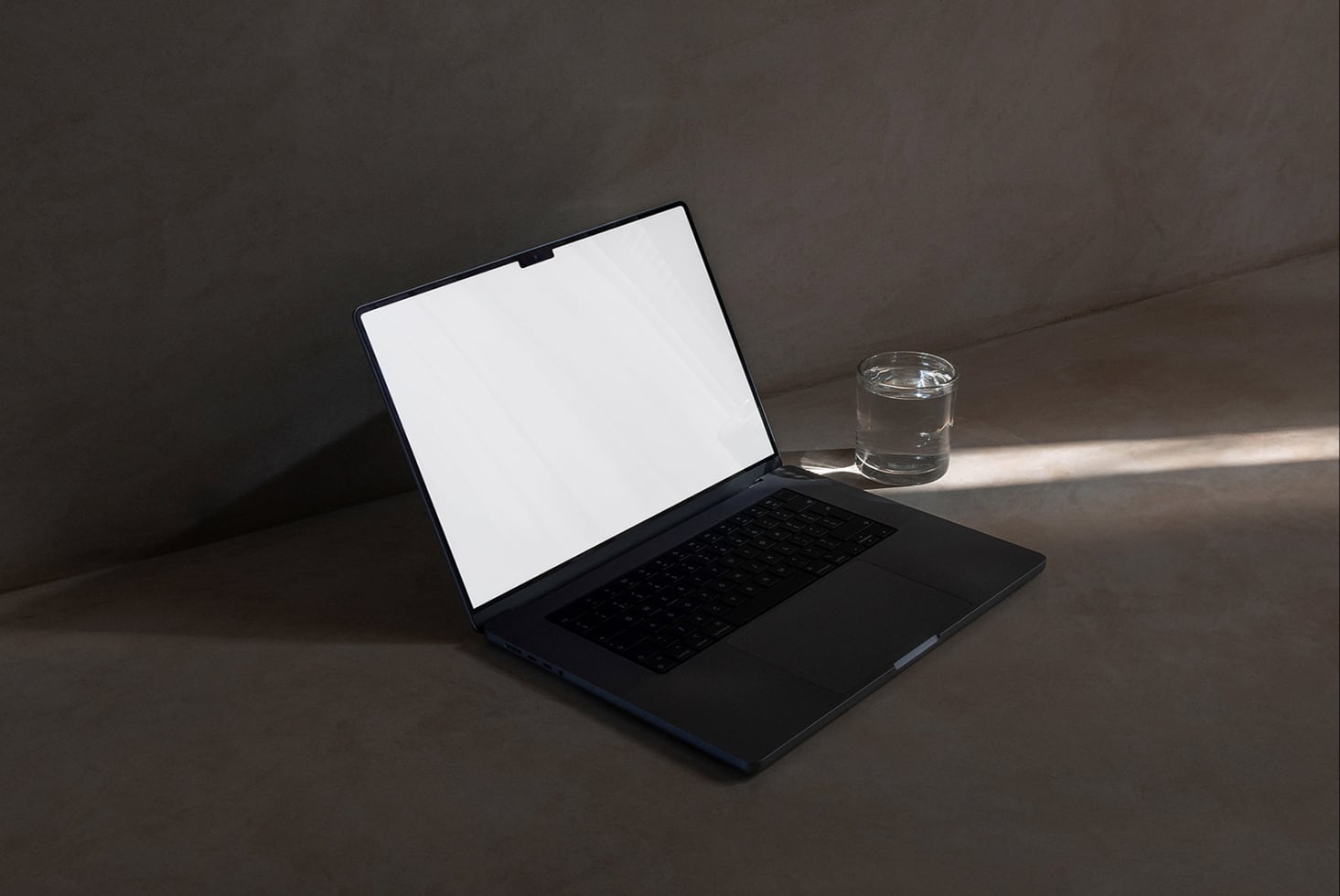 Black laptop with blank white screen next to glass of water on gray desk