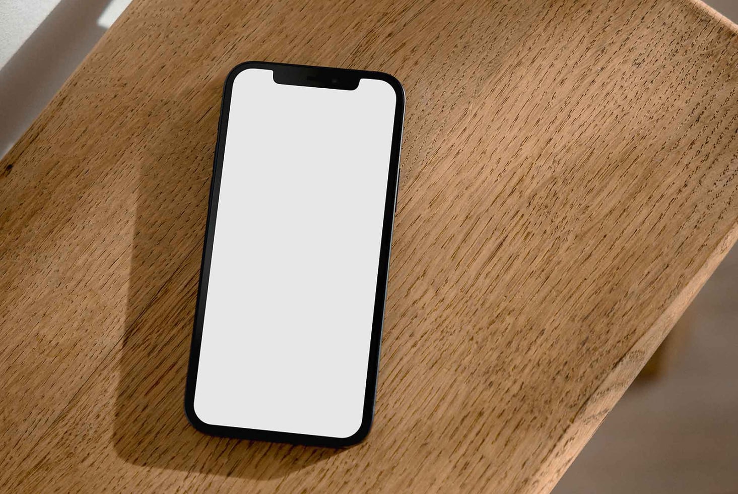 Blank white iPhone screen mockup resting on wooden surface with natural lighting