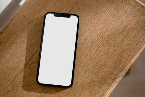Blank white iPhone screen mockup resting on wooden surface with natural lighting