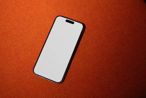Black iPhone on bright orange textured surface showing blank white screen mockup