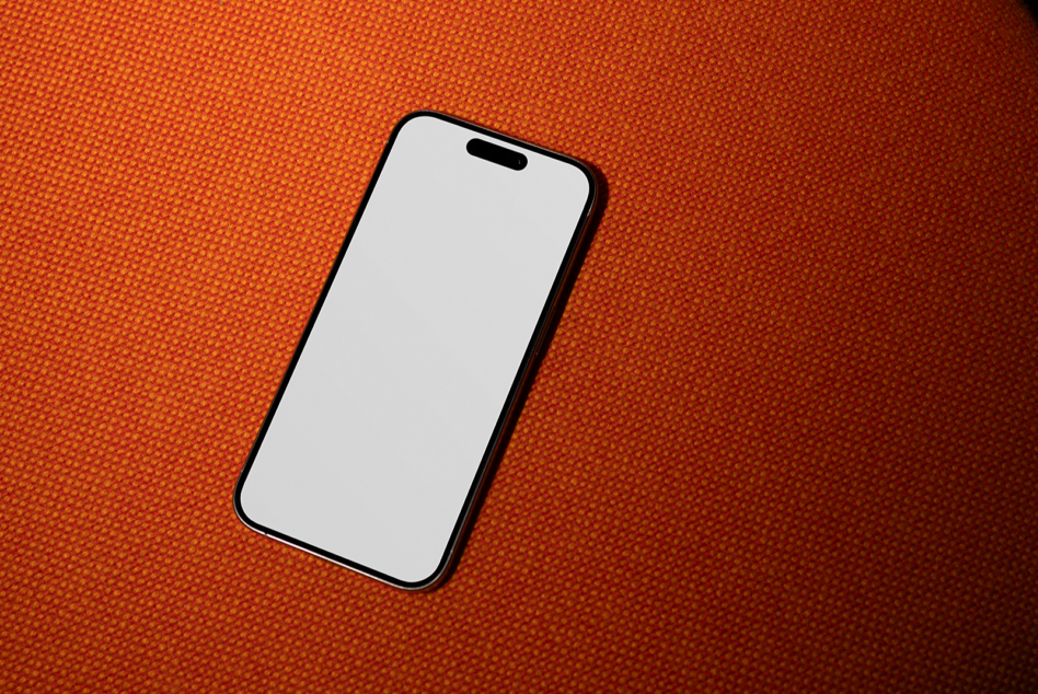 Black iPhone on bright orange textured surface showing blank white screen mockup