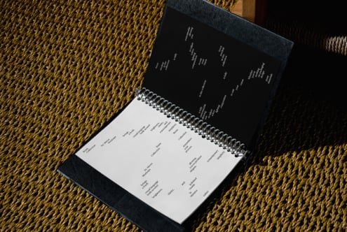 Spiral notebook with dark cover open on gold woven texture with wood frame