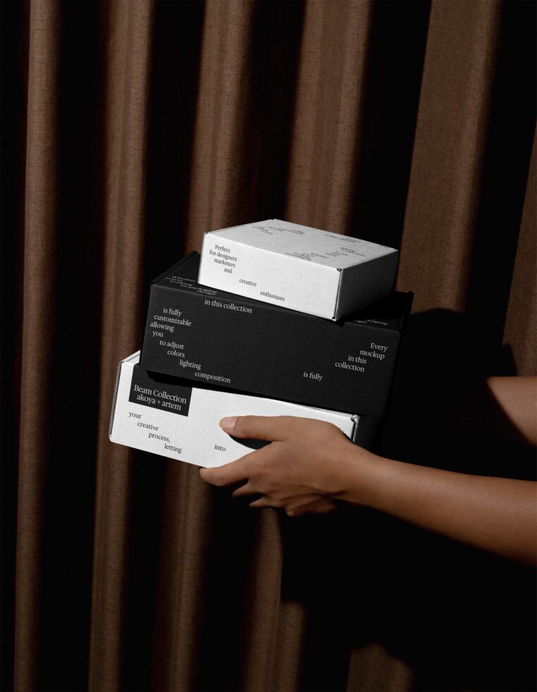 Stacked white, black, white boxes held in hands against draped curtain
