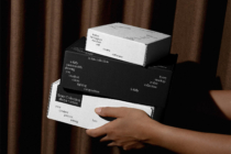 Stacked black plus white boxes held in hands with brown curtain background