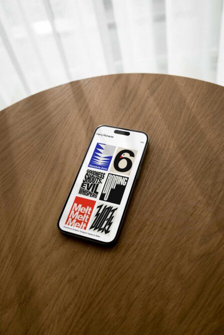 iPhone on wooden table showing portfolio site with typography color blocks layout