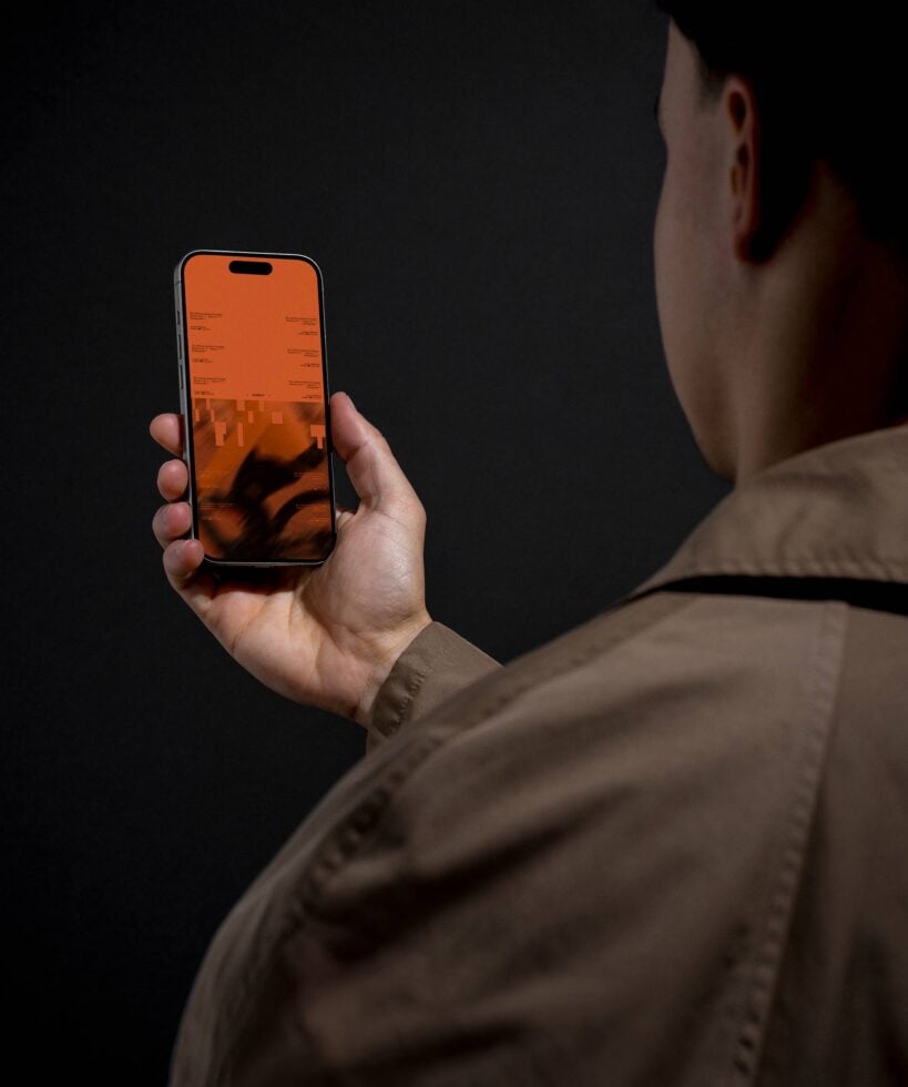 Person holding orange iPhone screen close to face against dark backdrop