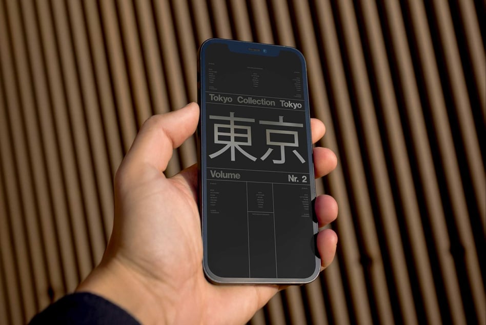 Hand holding dark blue phone showing Tokyo Collection dark mode layout