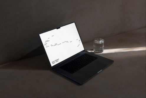 Black laptop displaying website layout with glass of water on gray desk
