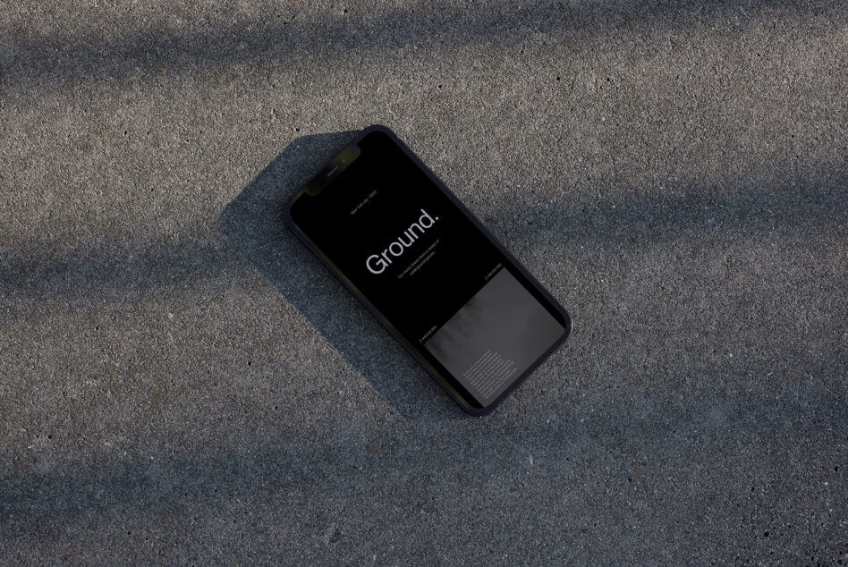 Black iPhone mockup displaying "Ground" app on concrete surface overhead shot