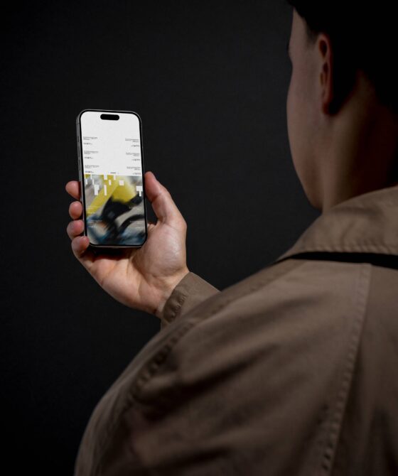 Person in brown jacket holding iPhone showing blurred yellow geometric design mockup