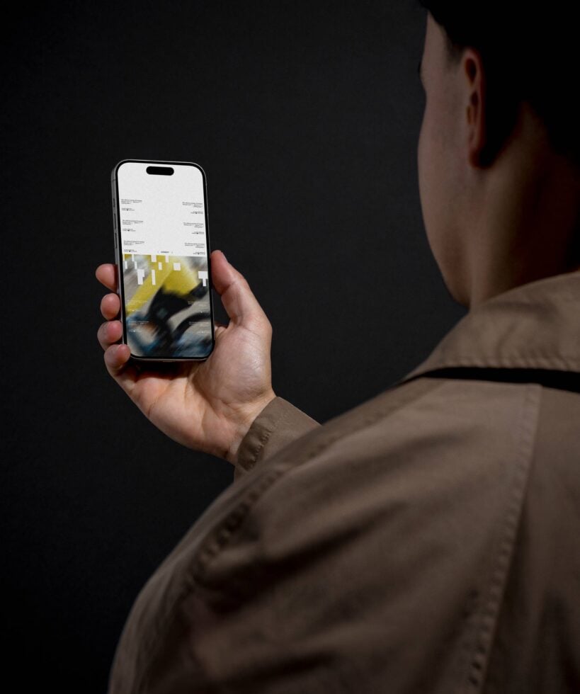 Person in brown jacket holding iPhone showing blurred yellow geometric design mockup