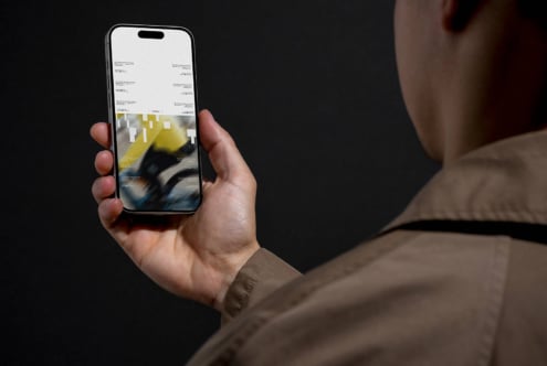 Person holding iPhone displaying website layout with yellow accent colors against dark