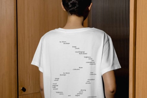 Back view of white tee with scattered text layout on wooden wall