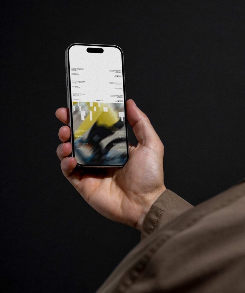 Hand holding iPhone displaying yellow design layout against black studio background