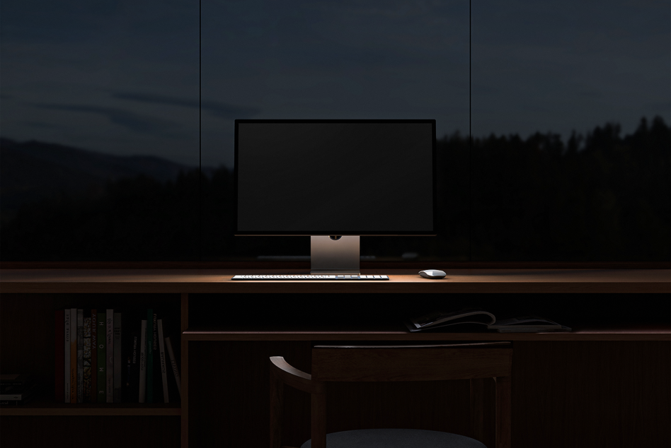 Workspace mockup featuring a minimalist office desk setup with a blank monitor, keyboard, and mouse in a dimly lit room; perfect for design presentations.