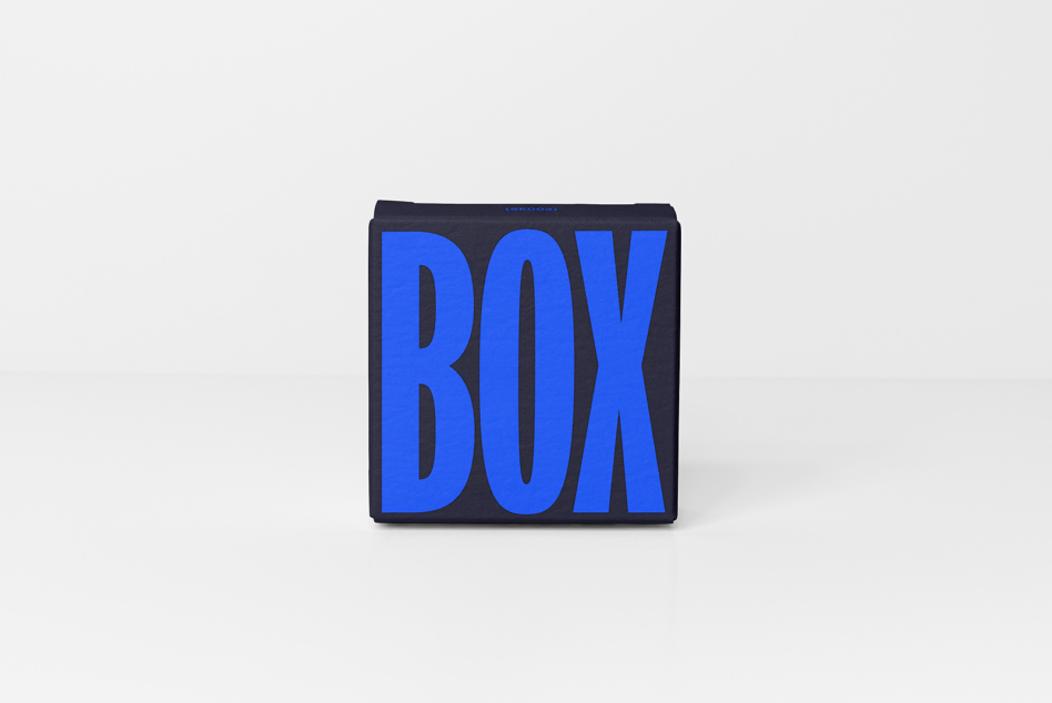 Dark charcoal box mockup with bright blue extruded lettering casting shadows on gray backdrop