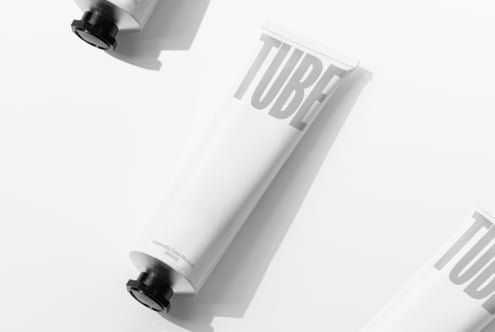 White cosmetic tube with black cap on angled surface showing embossed TUBE text