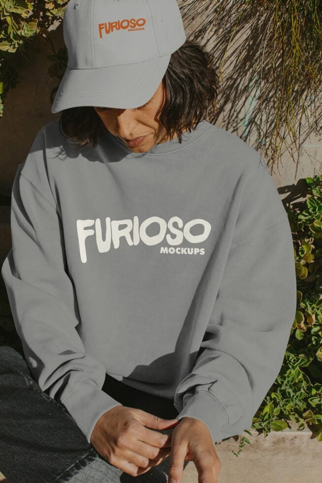 Person in light gray crewneck sweatshirt with white Furioso print under white cap