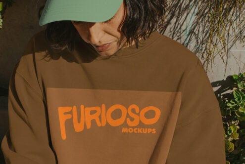 Close-up of tan crewneck with large orange Furioso text on front, person wearing mint cap
