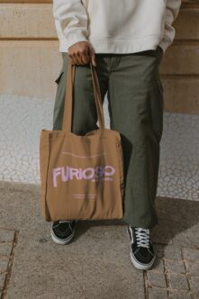 Caramel canvas tote with pink Furioso Mockups lettering in hand at street level