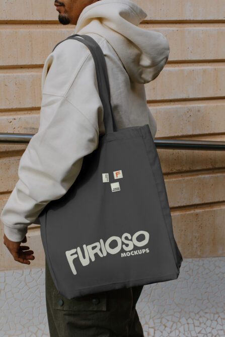 Black tote bag with large white Furioso Mockups logo worn over cream hoodie
