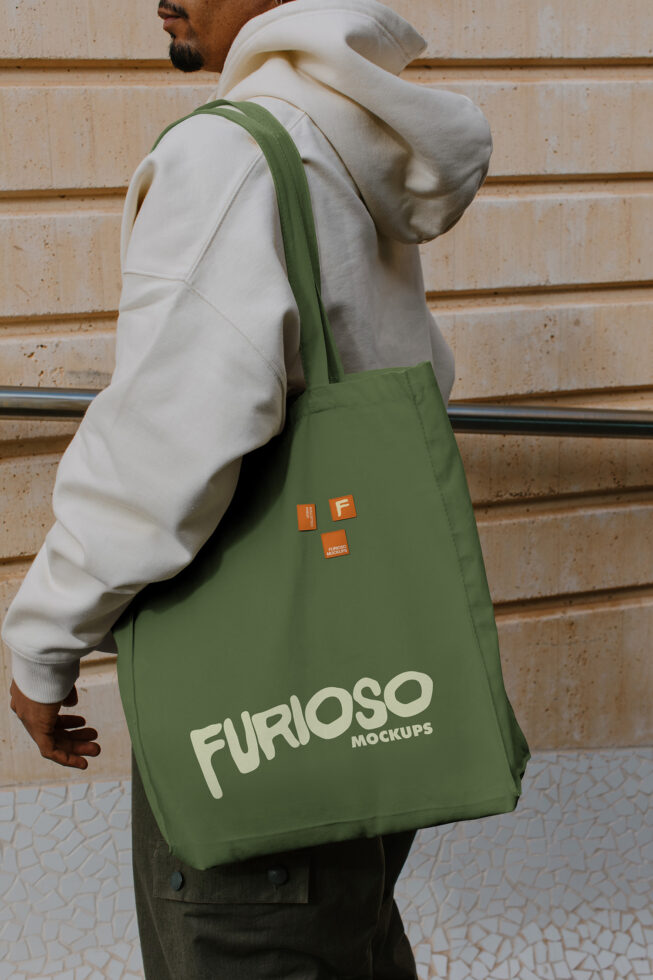 Man carrying olive green tote bag with cream Furioso Mockups text, orange logo patch visible