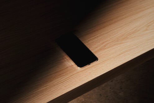 iPhone with blank black screen resting on light wood surface with soft shadows