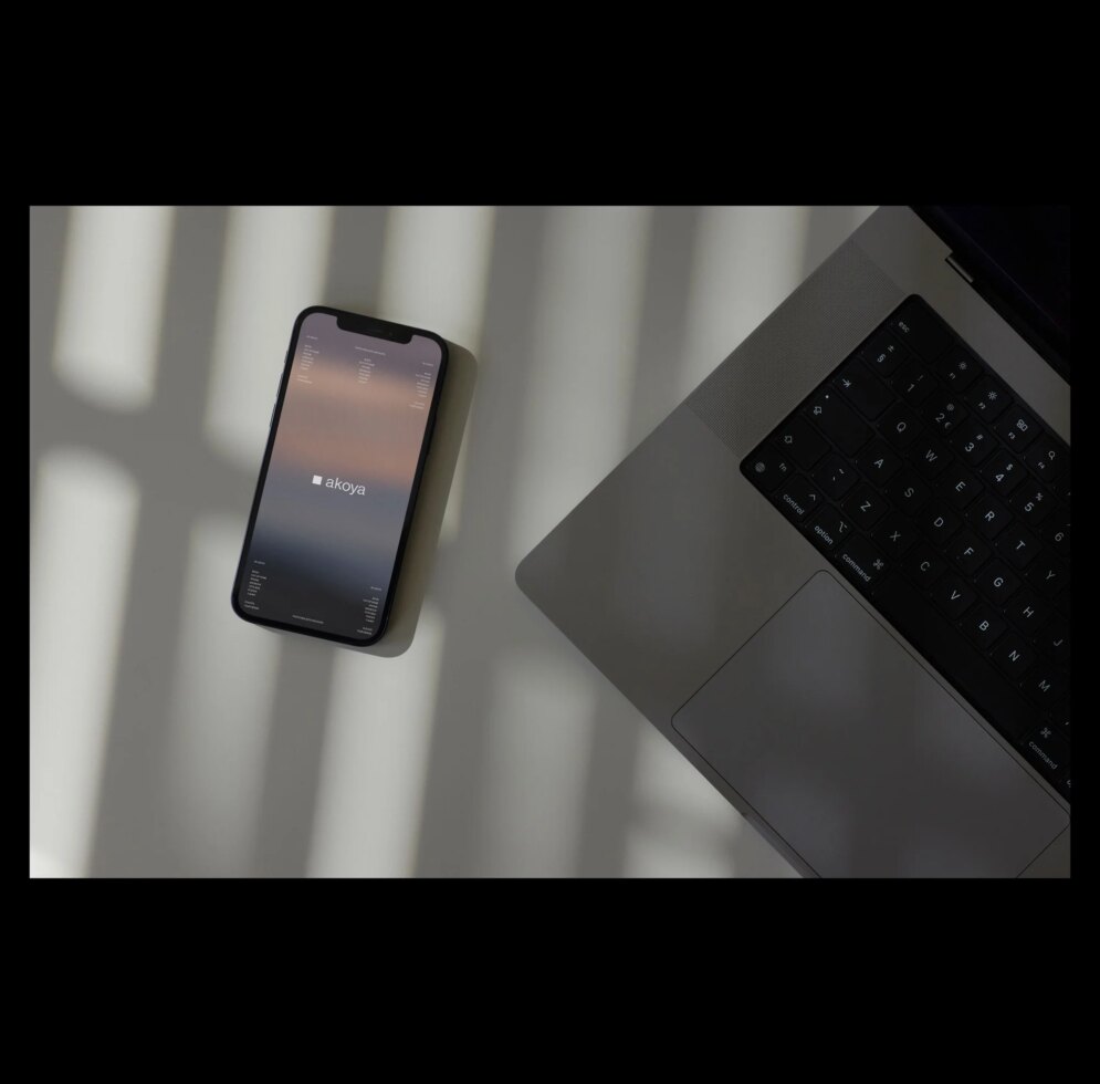 Phone and laptop on desk with sunlight; tech workspace mockup for designers; digital assets; creative layout; shadows; modern devices; minimalist design.