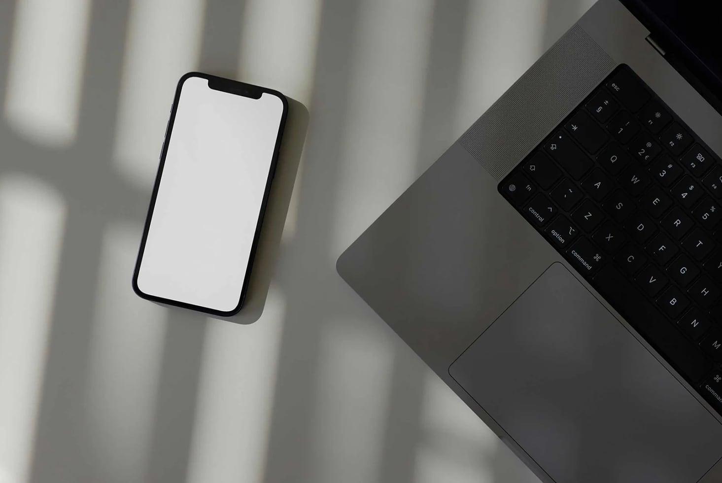Smartphone mockup with blank screen next to laptop on minimal desk with window shadows