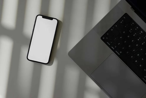 Smartphone mockup with blank screen next to laptop on minimal desk with window shadows
