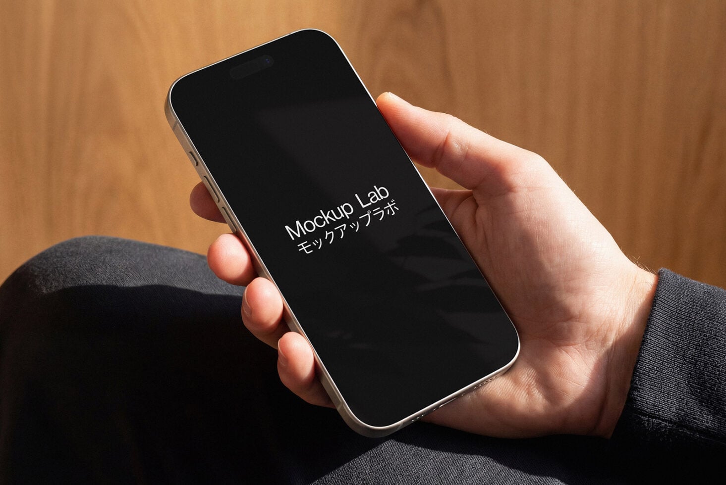 Person holding phone with black screen against warm wooden background