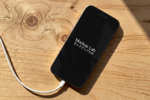 Black iPhone on wooden table displaying white Mockup Lab text with cable