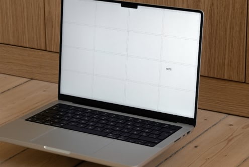 Silver laptop with white screen showing grid layout on wooden desk