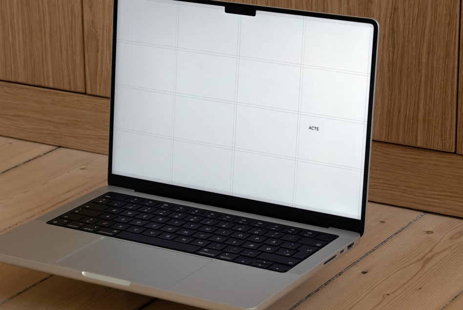 Silver laptop with white screen showing grid layout on wooden desk