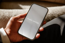 Hand holding phone with blank gray screen on beige fabric couch
