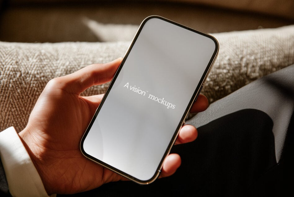 Hand holding phone with blank gray screen on beige fabric couch
