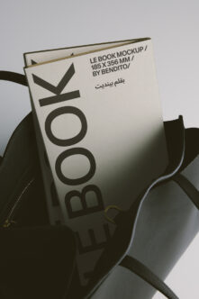 Cream book cover propped in black leather bag, soft product shot styling