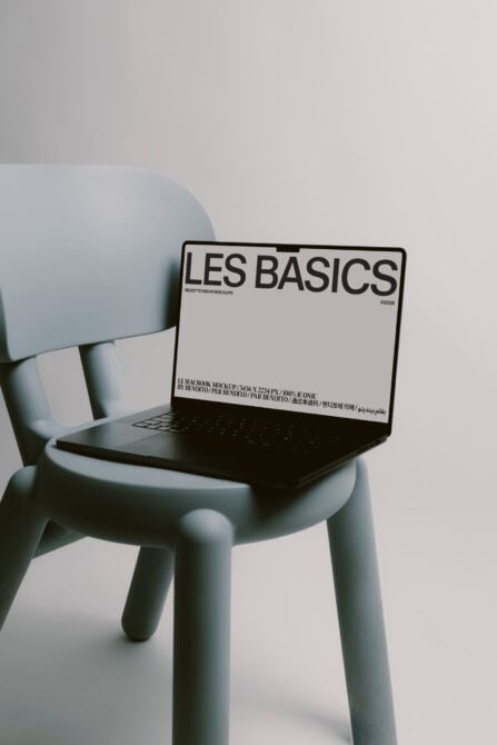 MacBook mockup on pale blue chair with Les Basics white screen layout visible