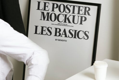 White poster in black frame showing Les Basics branding, styled with coffee on desk