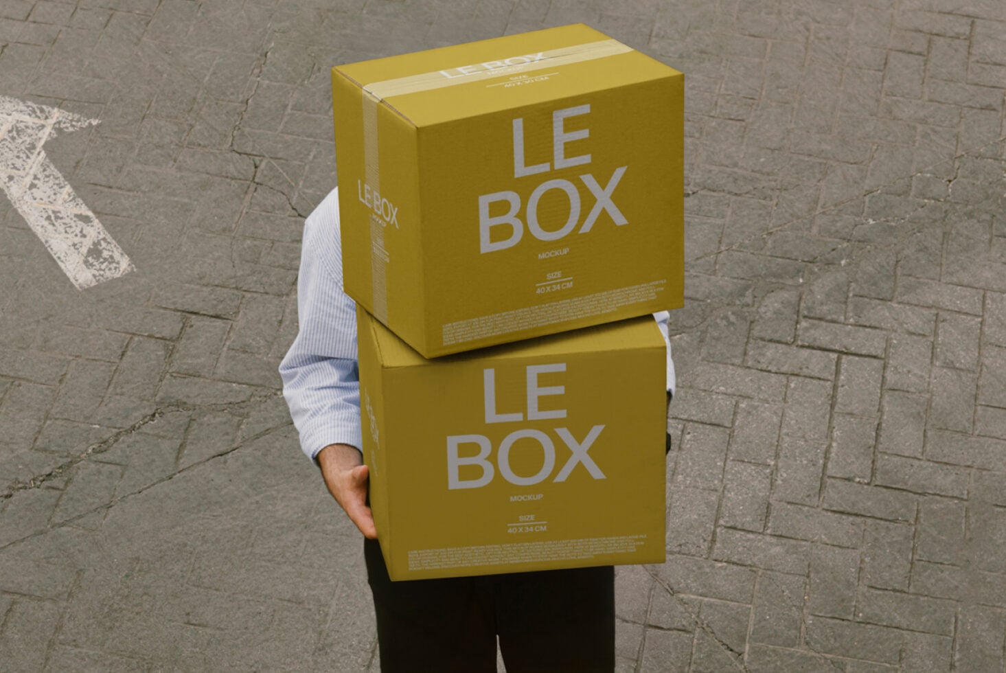 Person carrying two yellow cardboard boxes labeled LE BOX outdoors