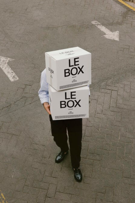 Person holding stacked white cardboard boxes labeled LE BOX on city street