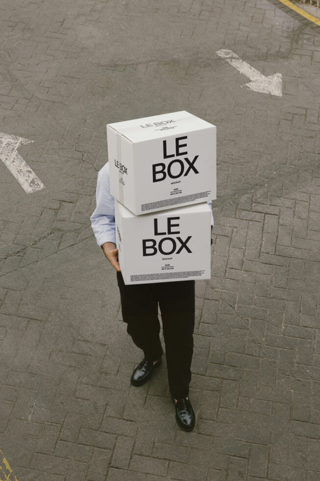 Person holding stacked white cardboard boxes labeled LE BOX on city street