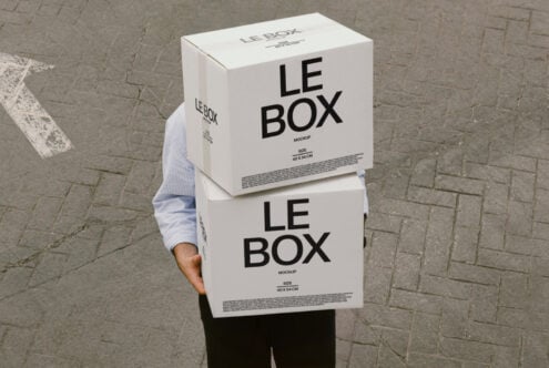 Person holding stacked white cardboard boxes labeled LE BOX on pavement