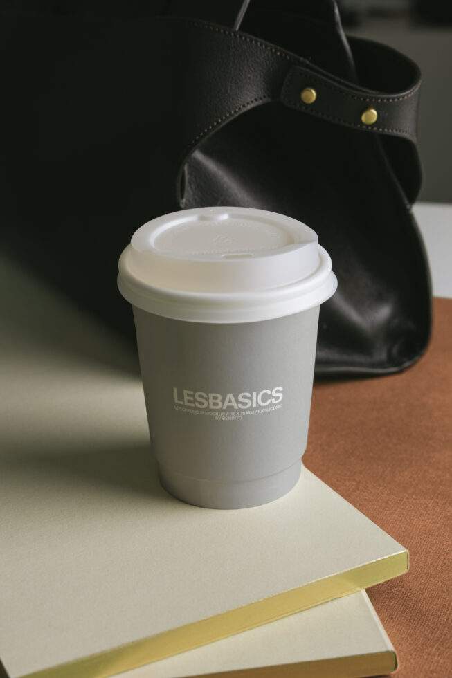 White coffee cup with lid styled on notebook beside black leather bag